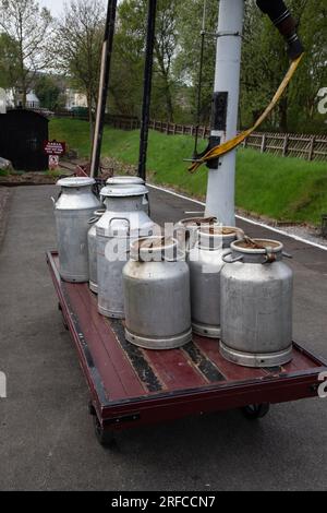 Traditional authentic tall conical and cylindrical milk churns on a wooden railway platform trolley at Oxenhope station on the K&WV Railway Stock Photo