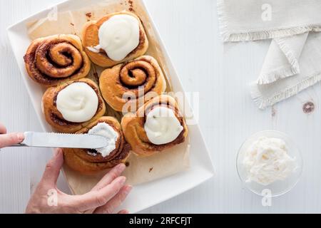 A close up of hands spreading frosting on a cinnamon bun. Stock Photo