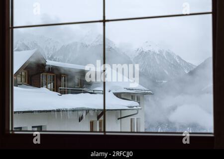 Winter landscape, view of the mountains outside the window. Winter Alps in fog and houses. Picture for background. Austria Stock Photo