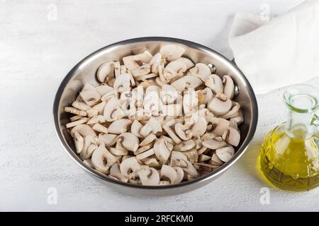 Frying pan with raw chopped champignons mushrooms on a light gray background. Stage of cooking a delicious vegetarian dish. Stock Photo