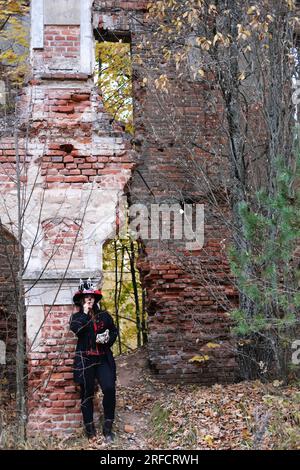 A woman in the image of Baron Saturday poses against the backdrop of an old abandoned building with a cigar in her hands. The model is dressed in a co Stock Photo