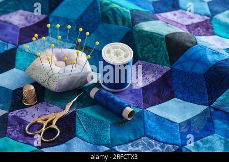 Pincushion, spools of thread, scissors and thimble on the tumbling blocks quilt background Stock Photo