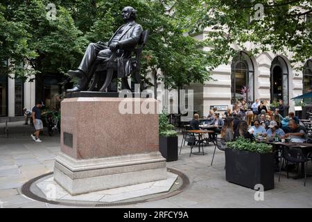 Outdoor restaurant customers sit at tables next to the statue of George Peabody in the City of London, the capital's financial district, on 26th July 2023, in London, England. George Peabody (1795 to 1869) was a philanthropist, banker and entrepreneur. Stock Photo