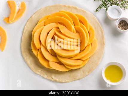 Rolled out dough with pumpkin filling surrounded by spices and olive oil on a white wooden background, top view. Cooking stage of delicious homemade p Stock Photo