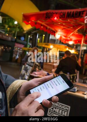 SMARTPHONE FOOD SHOPPNG BUYING LIST Mature male hand holding smartphone iPhone with interactive fruit and vegetable suggestions on-screen at dusk, shopping situation in Borough Market London UK Stock Photo