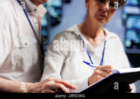 Aged colleagues monitoring server rows, optimizing them for data processing requirements of AI applications. Licensed experts working in high tech facility used for machine learning Stock Photo
