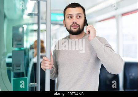 Young bearded man talking on phone in modern streetcar Stock Photo