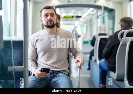 Young man with suitcase and smartphone riding in city bus Stock Photo