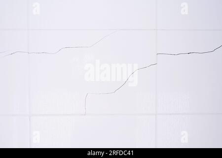 A white tiled wall with water droplets in the bathroom. Broken, cracked tiles. destroyed wall as a result of the earthquake Stock Photo