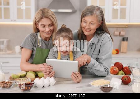 Three generations. Happy grandmother, her daughter and granddaughter using tablet in kitchen Stock Photo