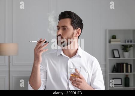 Man using cigarette holder for smoking and holding glass of whiskey in office Stock Photo