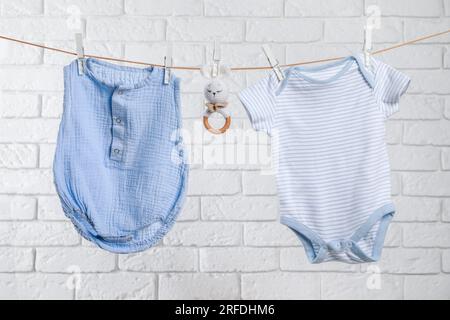 Cute baby onesies and crochet toy drying on washing line against white brick wall Stock Photo