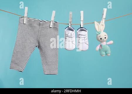 Striped baby pants, shoes and crochet toy drying on washing line against turquoise background Stock Photo