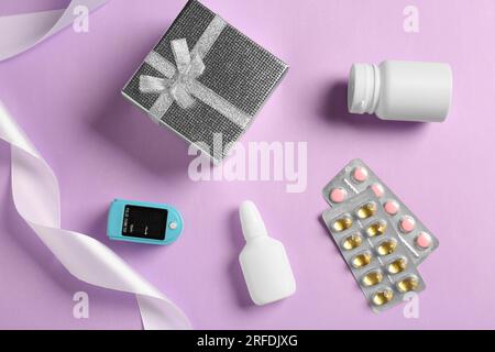 Spray bottle, pills, box and fingertip pulse oximeter on violet background, flat lay. Medical gift Stock Photo