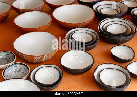 A large collection of handmade clay bowls in terra cotta, black, and white glaze in varying sizes. Sitting on a wood table in natural light. Stock Photo