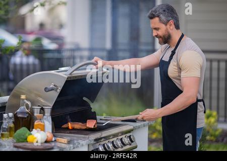 Male chef grilling and barbequing in garden. Barbecue outdoor garden party. Handsome man preparing barbecue meat. Concept of eating and cooking outdoo Stock Photo