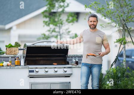 Barbecue concept. Middle aged hispanic man in t-shirt for barbecue. Roasting and grilling food. Roasting meat outdoors. Barbecue and grill. Cooking me Stock Photo