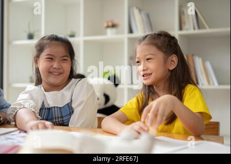 Two adorable young Asian girls are enjoying talking on a small break in a classroom together. children, kids, preschool, kindergarten students Stock Photo