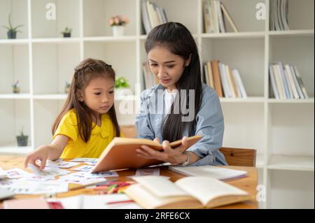 A pretty Asian preschool girl is studying the English alphabet on flashcards with a kind and caring female teacher. learning, studying, child developm Stock Photo