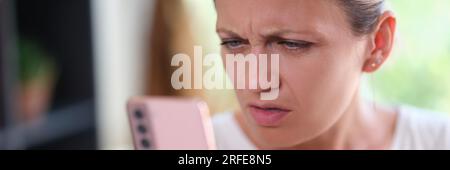 Woman with serious face looks doubtful at smartphone screen. . Stock Photo
