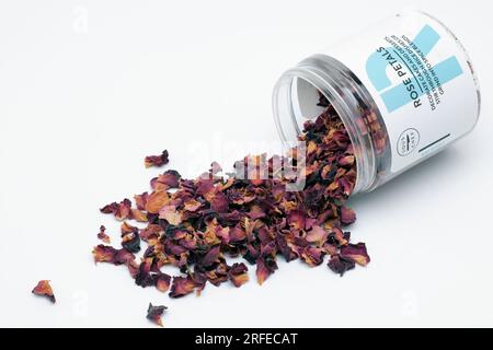 Plastic Container of Dried Rose Petals with Top Removed and Spilt onto a White Surface for Decorating Dishes and Desserts Stock Photo