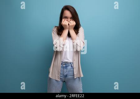 surprised puzzled 30s dark haired woman in shirt and jeans on blue background Stock Photo