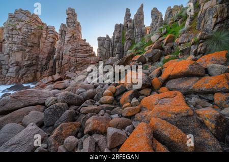 low angled view of lichen covered boulders, below towering sea stacks on a rugged coastline at Cape Woolamai on Phillip island in Victoria, Australia Stock Photo