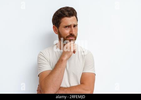 Handsome man holds his hand at his chin and looks thoughtfully at camera on white background Stock Photo