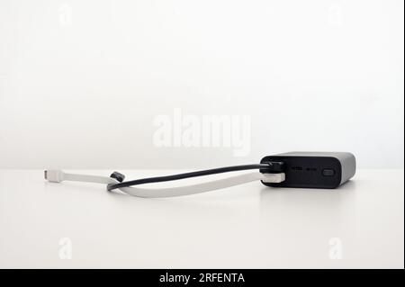 Black power bank on the table with two connected cables: black and white usb type-c cords. White background. Stock Photo