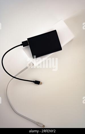 Black power bank on white mobile charger with white and black cord cable connected. White background. Stock Photo