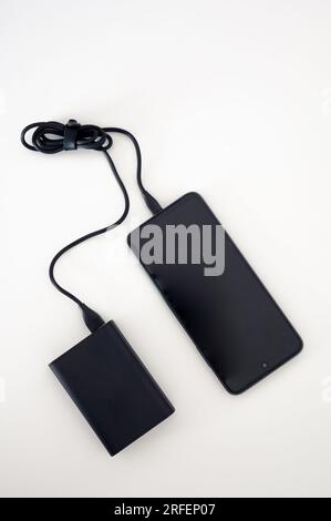 Black power bank charges black mobile phone. Mockup. Black cord cable. Both on the white background. Stock Photo