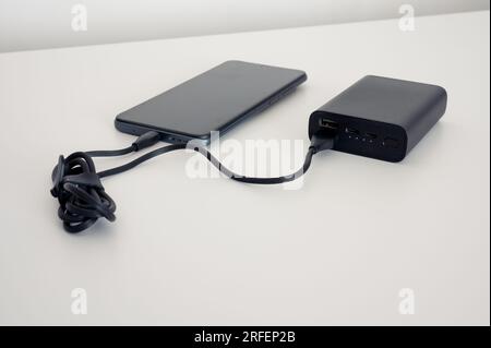 Black power bank charges mobile phone. Black cable. Both on the white background. Stock Photo