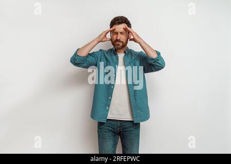 Man feeling sick, touching head and grimacing from painful headache standing on white background Stock Photo