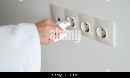 Hand inserts plug into socket closeup. Charging or plugging electrical appliances into socket Stock Photo
