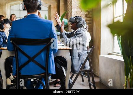 Teamwork colleagues using virtual reality headset inside business office - Multiracial people having fun with vr AI technology - Future and articifici Stock Photo