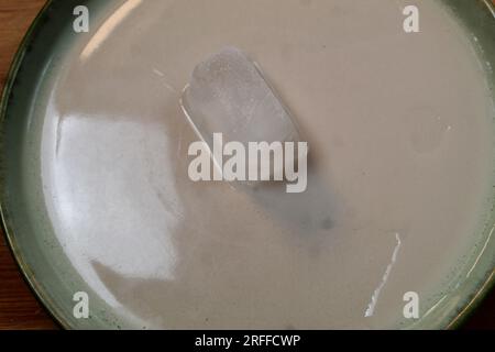A photo of an ice cube melting on a plate. Stock Photo