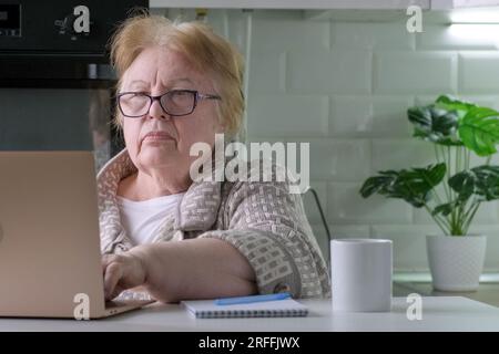 Older woman typing on laptop at home. Pensioner woman working at a computer Stock Photo