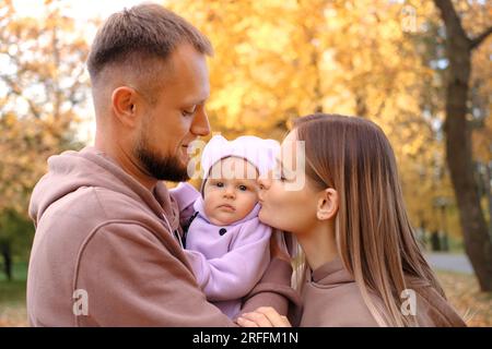 Young mother and father are walking with a newborn baby in the autumn park. Mother kissing newborn daughter Stock Photo