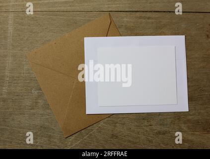 a blank white card on top of white and brown envelopes on a wooden table Stock Photo