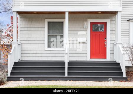 Detail of a front porch of a white home with grey steps leading up to a red door. Stock Photo
