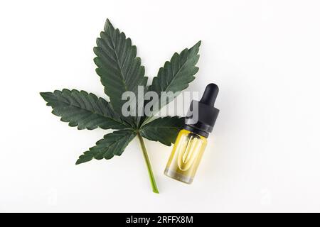 A green fresh leaf of medical marijuana, next to it is a glass vial of cbd oil extract with a dropper.  Cosmetic procedures using medical cannabis Stock Photo