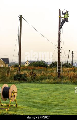 Technician attaching broadband fibre optic cable to a pole Stock Photo