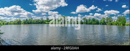 A small flat lake against the sky with clouds. Trees on the shore of the reservoir. Summer holidays, fishing Stock Photo
