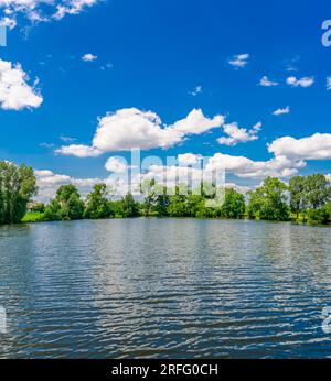 A small flat lake against the sky with clouds. Trees on the shore of the reservoir. Summer holidays, fishing Stock Photo