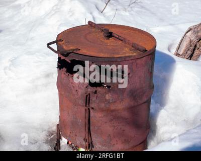 rusty barrel used as a stove for burning garbage, abandoned on the snow Stock Photo