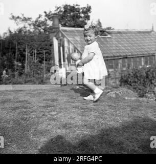 1950s, historical, summertime and an infant girl carrying her doll in a garden, England, UK. Stock Photo