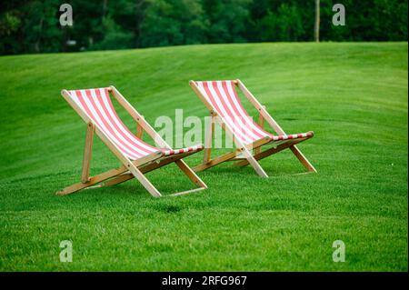 Two sun loungers on a fresh green lawn. A beautiful summer evening. Stock Photo