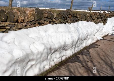 Snow drifts against a dry stone wall in Yorkshire, England. Stock Photo