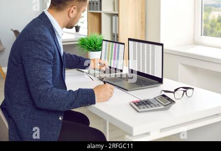 Man in office working with big data and databases using two laptops and excel tables. Stock Photo