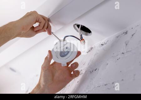 electrician installing recessed lamp in drywall ceiling. led lighting Stock Photo